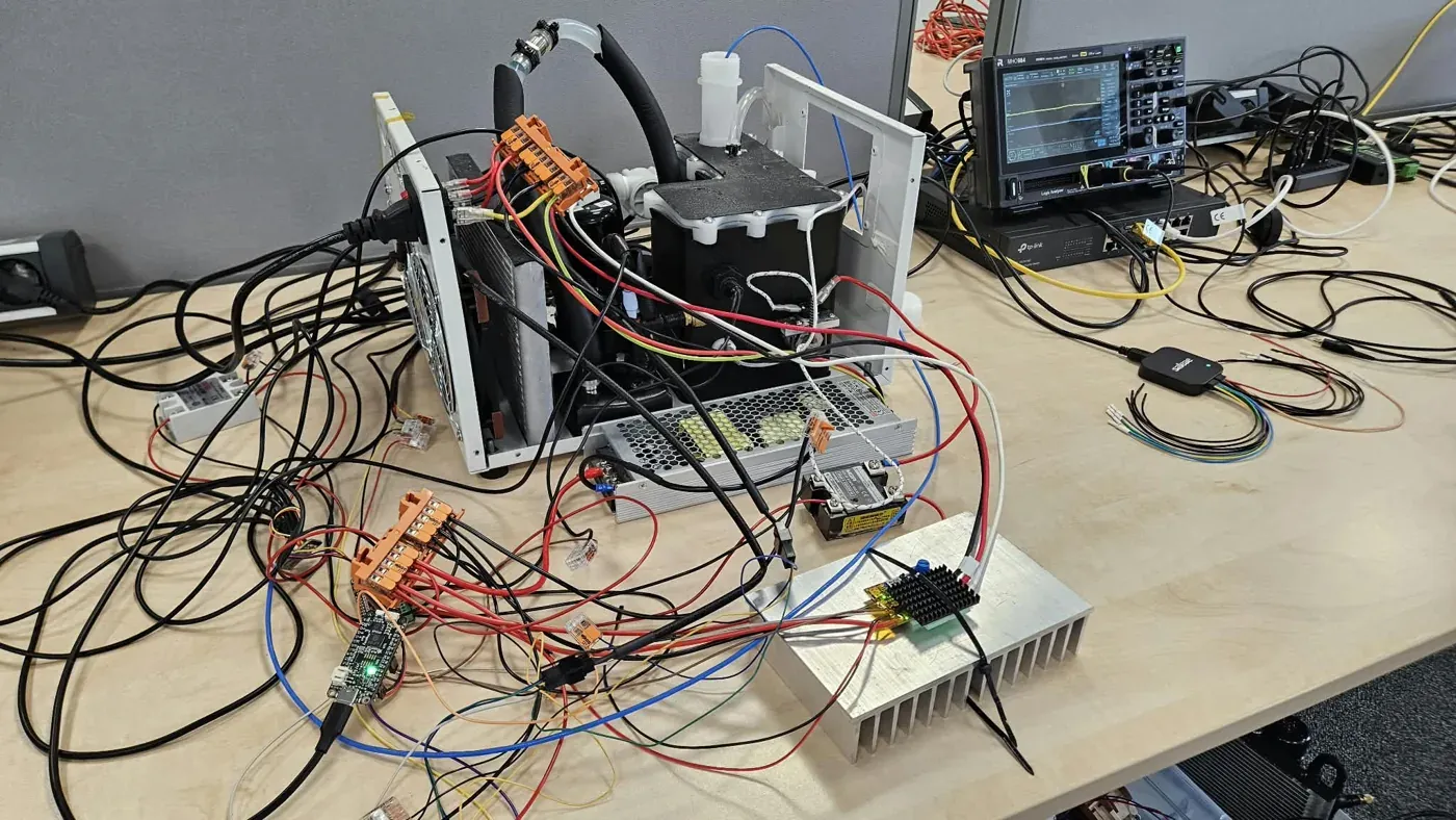 A benchtop bioprocess rig wired with power electronics, a heatsink, sensors and a fluidic head, instrumented on a lab bench.